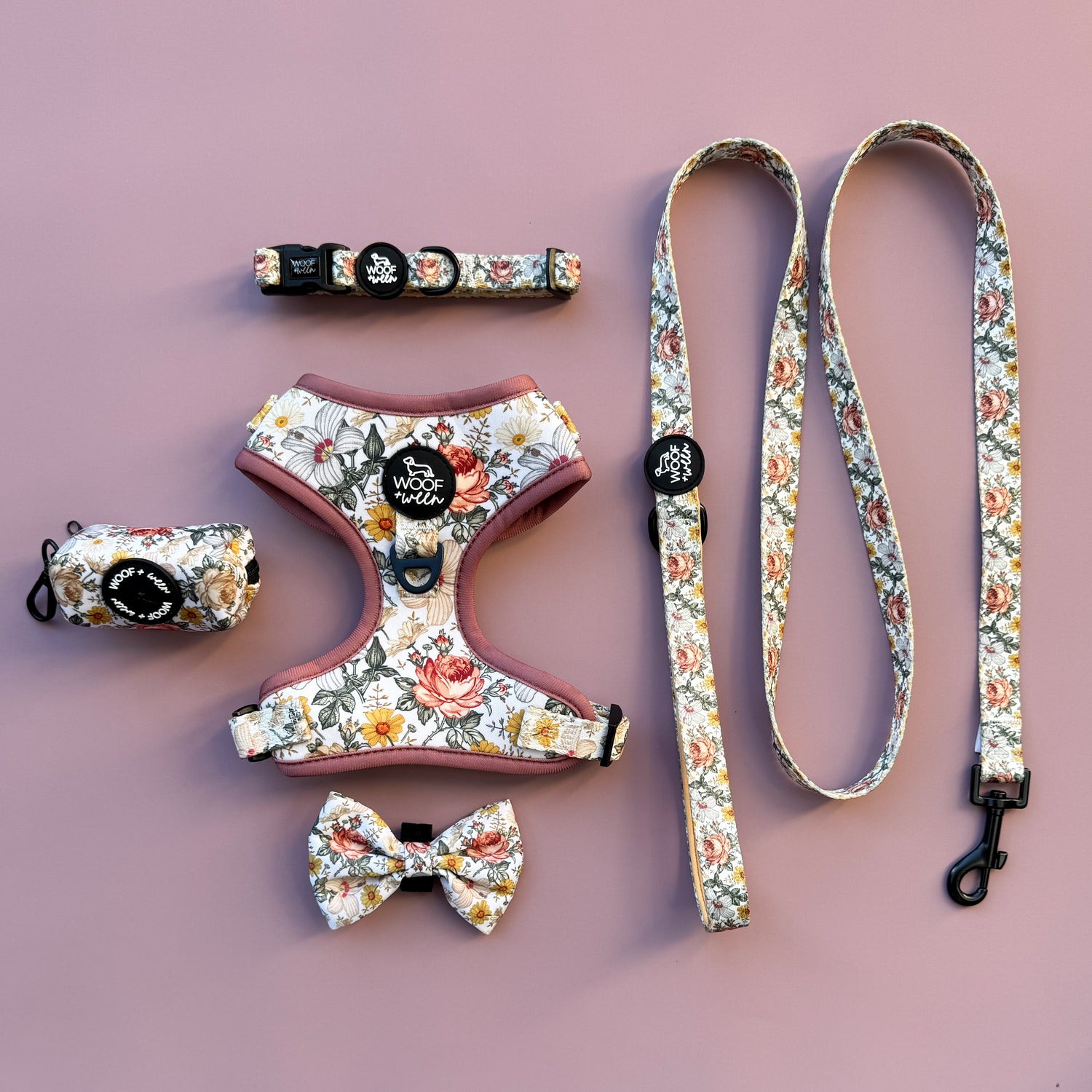 Floral dog harness, leash, collar, and bow tie set on a pink background