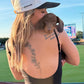 A woman at a baseball game wearing a white and black woof+ween trucker hat with 'hot girls have wiener dogs” embroidered on it