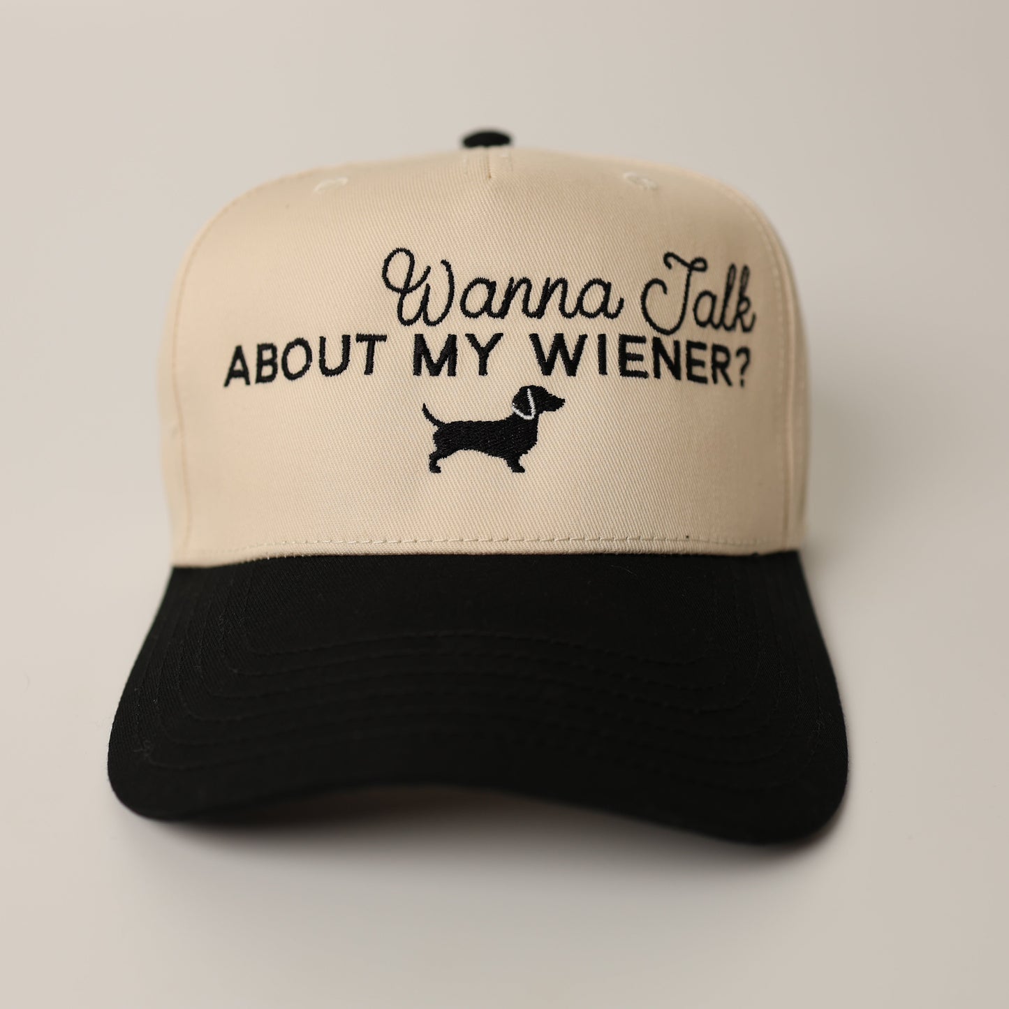 Beige and black cap with text 'Wanna Talk About My Wiener?' on a beige background