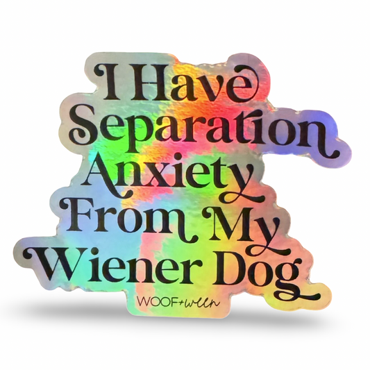 A die-cut sticker with the text 'I Have Separation Anxiety From My Wiener Dog' in black script, featuring a holographic rainbow sheen and the brand name 'WOOFwith' at the bottom, shown on a white background.