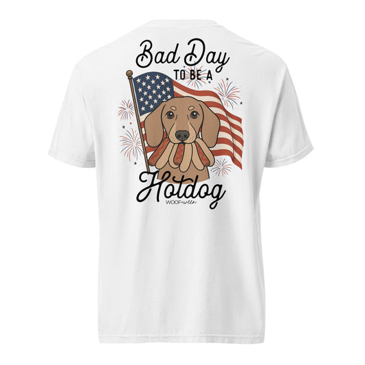 White t-shirt with a graphic of a dog eating hotdogs and an American flag and text 'Bad Day to be a Hotdog' on a white background.