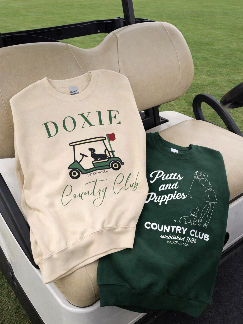 Two sweatshirts with 'Doxie Country Club' and 'Putts and Puppies Country Club' designs on a golf cart seat.
